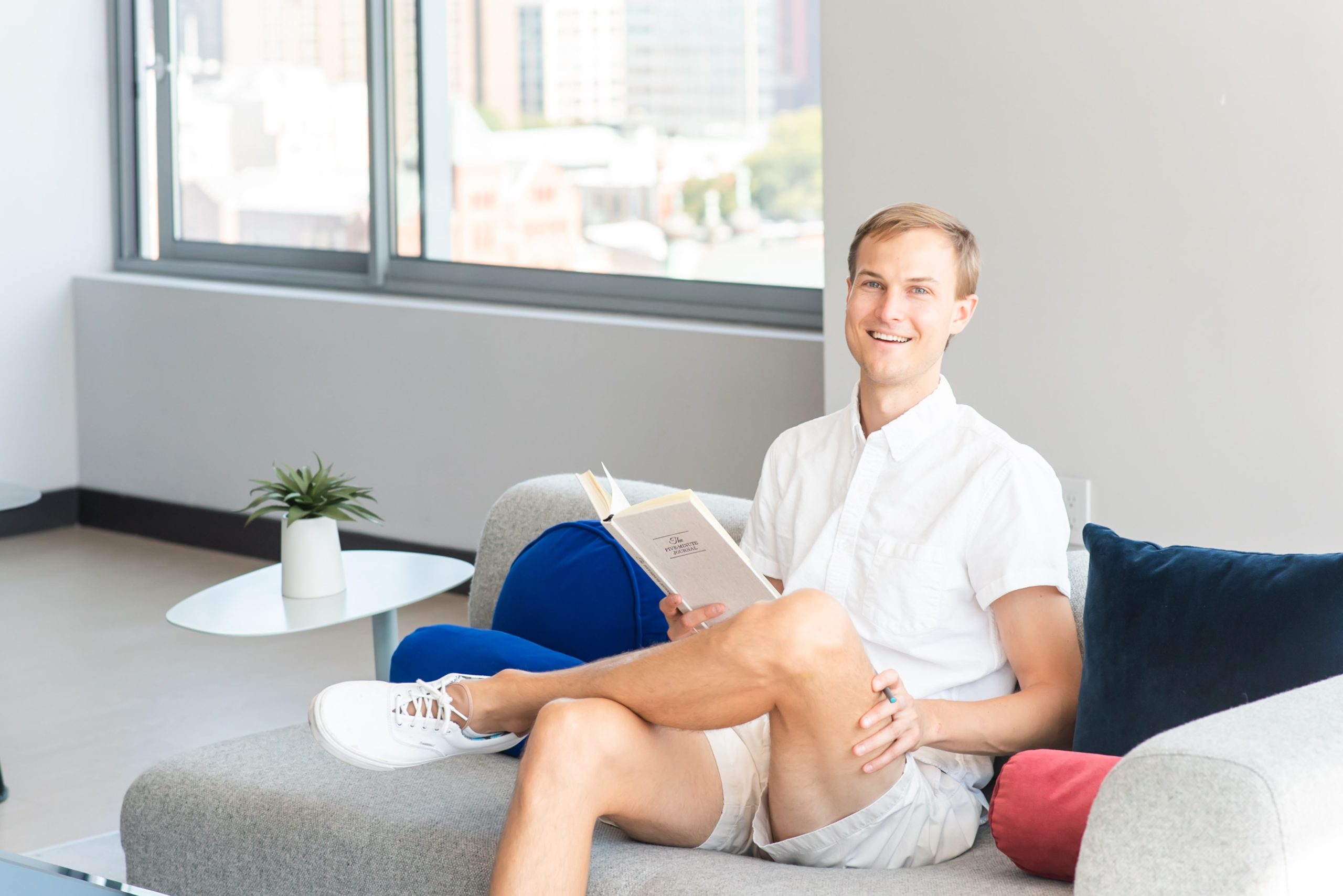 Austin Belcak sitting on couch smiling and reading a book